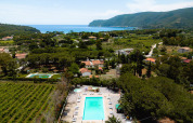 Aerial view of Camping Casa dei Prati holiday park in Tuscany, Italy, showing pool, trees, and sea in the distance.