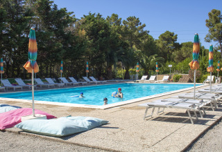 Buitenzwembad met ligstoelen en kleurrijke parasols bij Camping Casa dei Prati in Toscane, Italië.