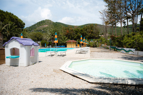 Zona de piscina familiar con tumbonas, sombrillas de colores y casita de juegos en Camping Casa dei Prati, Toscana.