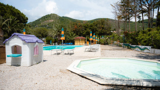 Zona de piscina familiar con tumbonas, sombrillas de colores y casita de juegos en Camping Casa dei Prati, Toscana.