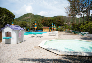 Zona de piscina familiar con tumbonas, sombrillas de colores y casita de juegos en Camping Casa dei Prati, Toscana.