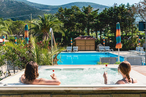 Due persone si rilassano in una vasca idromassaggio con vista sulla piscina e le montagne al Camping Casa dei Prati in Toscana.