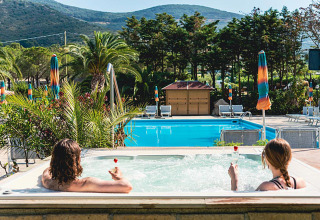 Twee mensen ontspannen in een bubbelbad met uitzicht op het zwembad en de bergen bij Camping Casa dei Prati in Toscane.