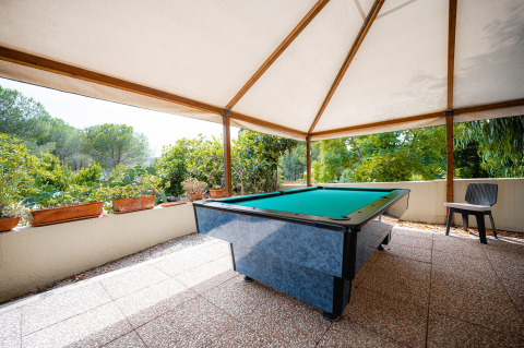 Mesa de billar exterior bajo toldo con vistas a la vegetación en Camping Casa dei Prati, Toscana, Italia.