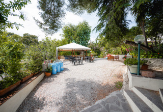 Udendørs opholdsområde med pavillon, stole og borde omgivet af frodige træer på Camping Casa dei Prati i Toscana.