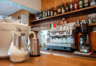 Zona de bar con cafetera, tazas, vasos y botellas en Camping Casa dei Prati, en la Toscana, Italia.