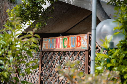 Ingang van de MINI CLUB bij Camping Casa dei Prati, een gezinsvakantiepark omgeven door planten in Toscane.