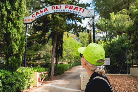 Mujer con gorra verde neón mira la entrada del Camping Casa dei Prati en la Toscana, Italia.
