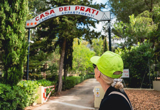 Vrouw met neon groene pet kijkt naar de ingang van Camping Casa dei Prati in Toscane, Italië.