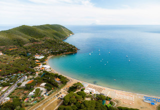 Vista aerea del Camping Casa dei Prati con spiaggia sabbiosa, colline verdi e barche in Toscana, Italia.