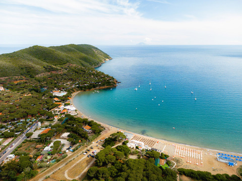 Vista aerea del Camping Casa dei Prati con spiaggia sabbiosa, colline verdi e barche in Toscana, Italia.