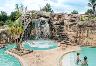 Holiday park pool with waterfall, rocks and palm trees at Camping Castel L'Orangerie de Lanniron, Brittany, France.