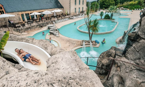 Un tobogán acuático y piscinas rodeadas de palmeras en Camping Castel L'Orangerie de Lanniron, Bretaña, Francia.