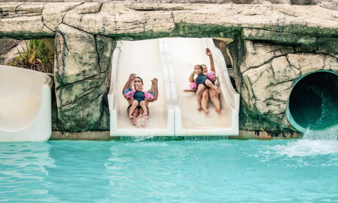 Niños disfrutando en un tobogán doble en la piscina de Camping Castel L'Orangerie de Lanniron, Bretaña, Francia.