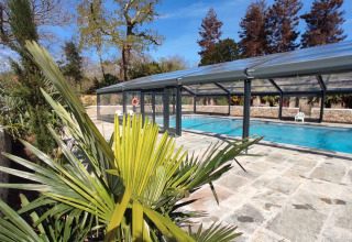 Udendørs swimmingpool med glastag, omgivet af træer og planter i solskin på L'Orangerie de Lanniron, Bretagne.