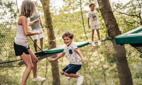 Niños y adultos juegan juntos en una red de trampolín al aire libre en Camping L'Orangerie de Lanniron, Bretaña.