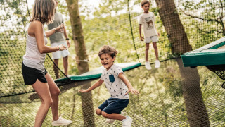 Kinder und Erwachsene spielen auf einem Outdoor-Trampolin zwischen Bäumen im Ferienpark L'Orangerie de Lanniron.