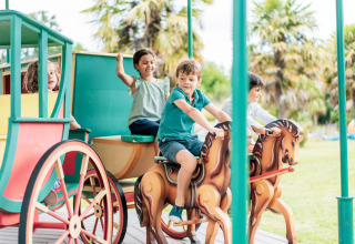 Bambini che giocano e cavalcano cavalli da giostra nel parco giochi di Camping Castel L'Orangerie de Lanniron.