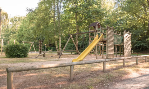 Speelplein met houten structuren en gele glijbaan op Camping Castel L'Orangerie de Lanniron, Bretagne, Frankrijk.