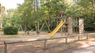 Spielplatz mit Holzstrukturen und Rutsche im Grünen im Camping Castel L'Orangerie de Lanniron, Bretagne, Frankreich.