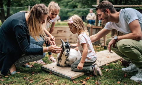 A family pets a goat outdoors at Camping Castel L'Orangerie de Lanniron, a holiday park in Brittany, France.