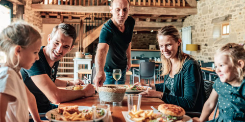 Famiglia che gusta un pasto insieme in un ristorante rustico a Camping Castel L'Orangerie de Lanniron, Bretagna, Francia.