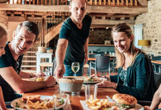 Famiglia che gusta un pasto insieme in un ristorante rustico a Camping Castel L'Orangerie de Lanniron, Bretagna, Francia.
