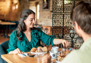 En kvinde og en mand nyder morgenmad i en hyggelig restaurant på Camping Castel L'Orangerie de Lanniron i Bretagne.