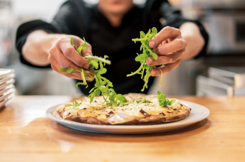 Un chef agrega rúcula fresca a una pizza en la cocina de Camping Castel L'Orangerie de Lanniron, Bretaña, Francia.