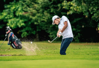 Een golfspeler slaat een bal uit een bunker op Camping Castel L'Orangerie de Lanniron in Bretagne, Frankrijk.