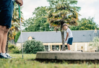 En lille dreng spiller minigolf med en voksen ved en feriepark med palmetræer i Bretagne, Frankrig.