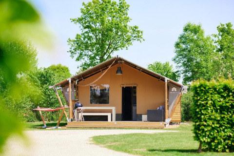 Tienda de safari Villatent Nomad con terraza, barbacoa y hamaca rodeada de árboles y naturaleza verde.