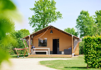 Tienda de safari Villatent Nomad con terraza, barbacoa y hamaca rodeada de árboles y naturaleza verde.