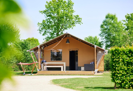 Tienda de safari Villatent Nomad con terraza, barbacoa y hamaca rodeada de árboles y naturaleza verde.