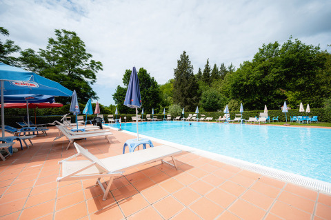 Piscina al aire libre en Camping Colleverde en la Toscana, Italia, rodeada de tumbonas y sombrillas azules.