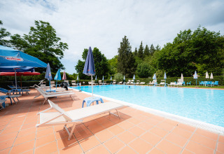 Outdoor swimming pool at Camping Colleverde in Tuscany, Italy, with sun loungers and umbrellas around it.