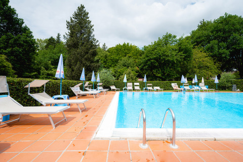 Freibad im Camping Colleverde in der Toskana, Italien, mit Liegestühlen und viel grünem Baumbestand.