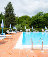 Freibad im Camping Colleverde in der Toskana, Italien, mit Liegestühlen und viel grünem Baumbestand.