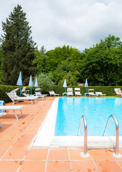 Freibad im Camping Colleverde in der Toskana, Italien, mit Liegestühlen und viel grünem Baumbestand.