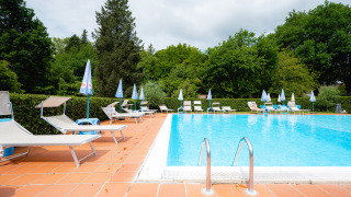 Piscina exterior en Camping Colleverde en la Toscana, Italia, rodeada de tumbonas y árboles verdes.