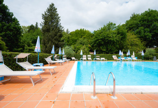 Freibad im Camping Colleverde in der Toskana, Italien, mit Liegestühlen und viel grünem Baumbestand.