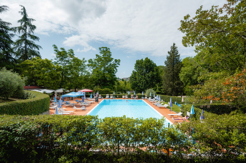 Piscina al aire libre rodeada de tumbonas y sombrillas en Camping Colleverde, parque vacacional en la Toscana, Italia.