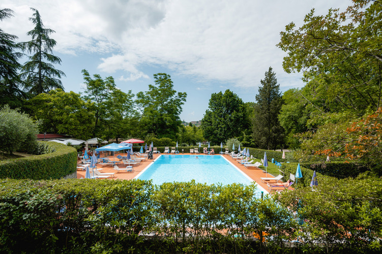 Outdoor swimming pool with sun loungers and umbrellas at Camping Colleverde holiday park in Tuscany, Italy.