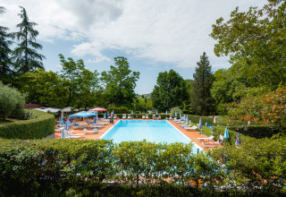 Piscina al aire libre rodeada de tumbonas y sombrillas en Camping Colleverde, parque vacacional en la Toscana, Italia.