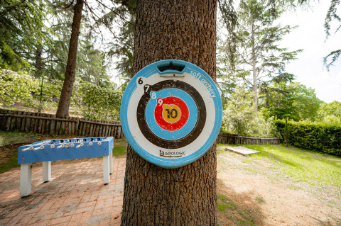 Bersaglio blu e bianco su un albero al Camping Colleverde, Toscana, con calcio balilla in giardino.