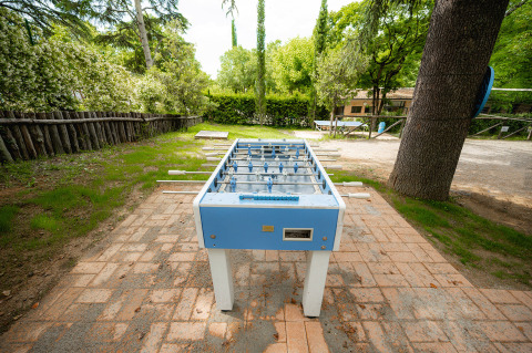 Mesa de futbolín al aire libre en Camping Colleverde, rodeada de árboles y vegetación en la Toscana, Italia.