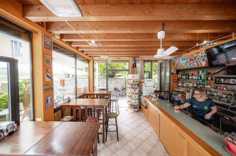 Caffetteria luminosa con soffitto in legno e bar al Camping Colleverde, Toscana, Italia. Staff serve caffè.
