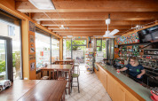 Lys café med træloft og bar på Camping Colleverde i Toscana, Italien. Person serverer kaffe bag disken.