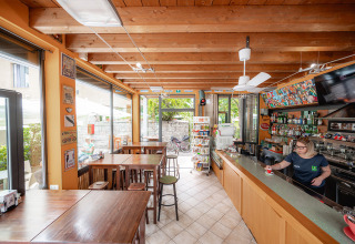 Caffetteria luminosa con soffitto in legno e bar al Camping Colleverde, Toscana, Italia. Staff serve caffè.