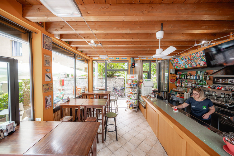 Bright café with wooden ceiling and bar at Camping Colleverde, Tuscany, Italy. Staff serving coffee at counter.
